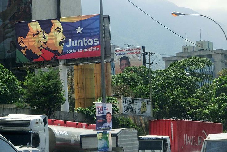 Straße mit übermäßig vielen Wahlplakaten. Auf dem zentralen das schneidige Gesicht Maduros und Hugo Chavez im Profil.