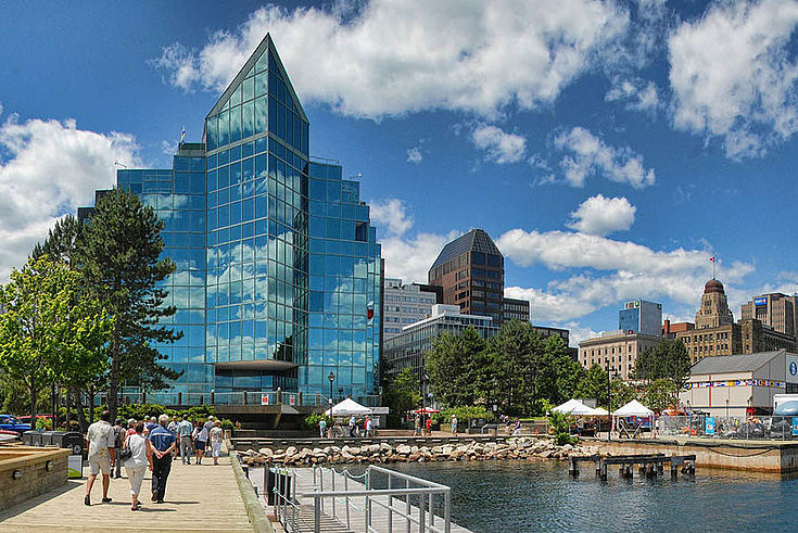 Halifax. Wasser zur Rechten (wahrscheinlich ein künstlicher Teich), dort auch hoher Flaggenmast mit der Kanada-Flagge. Links ein verglaster Bürobau.