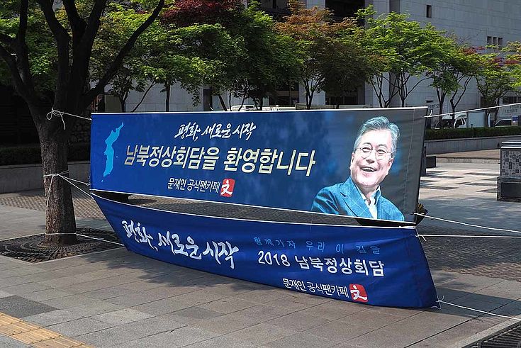 Über eine Straße gespanntes Plakat mit dem lachenden Gesicht von Moon Jae-In