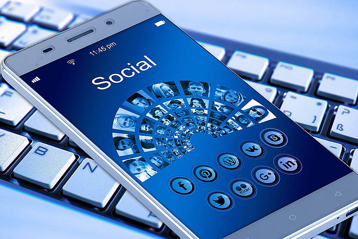 Themenbild eines Handys auf einer Tastatur. Auf dem Bildschirm steht: "Sozial"