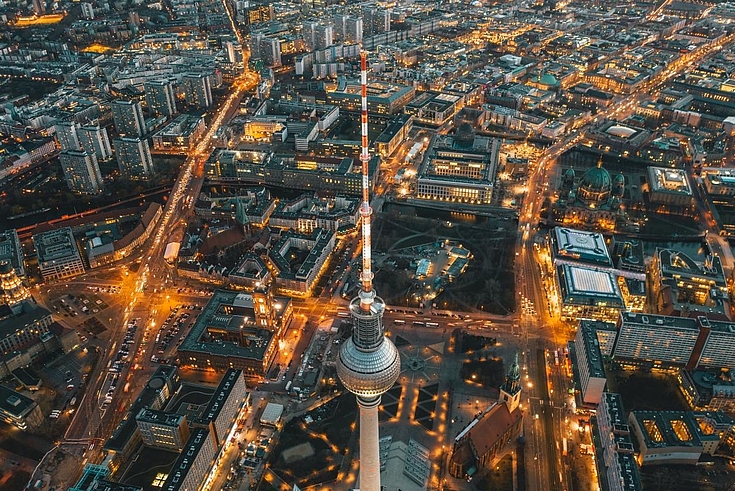Der Berliner Fernsehturm von oben. Unten leuchten belebte Straßen. 